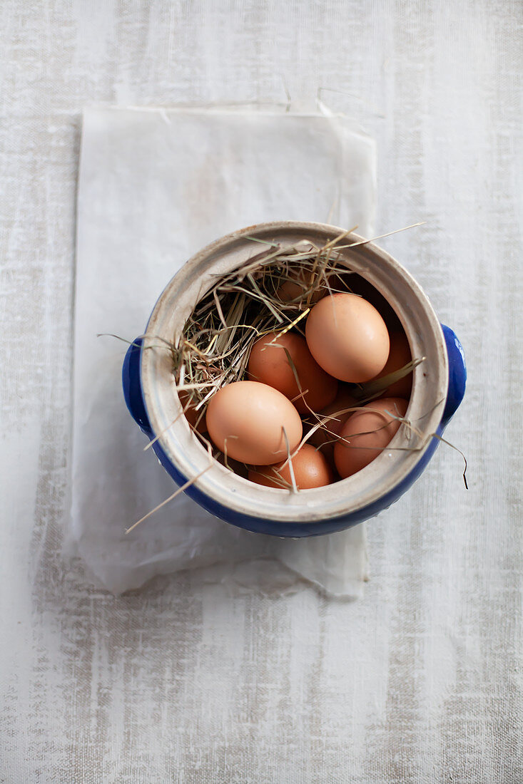 Hay and brown eggs in stoneware pot