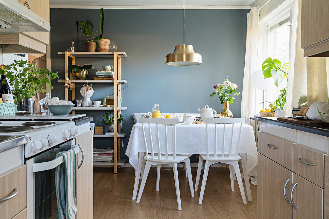 Blick aus der offenen Küche auf den gedeckten Tisch vor blauer Wand