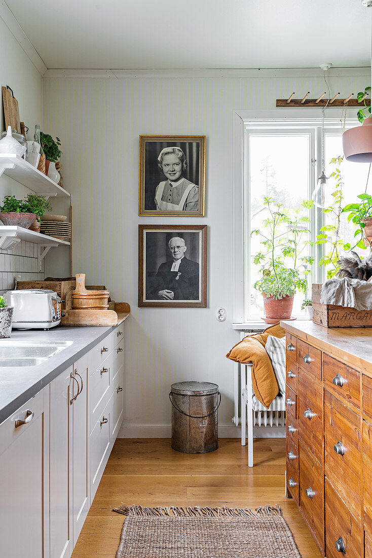Kitchen island made from old shop counter in white kitchen with black-and-white photo portraits on wall