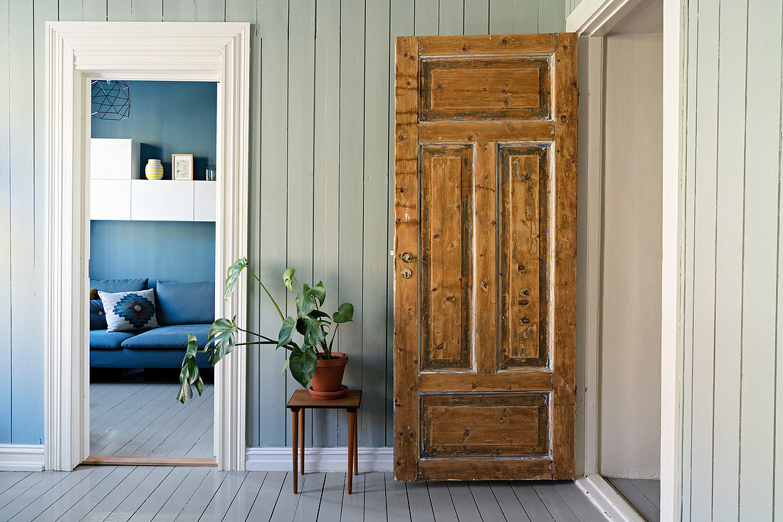 Rustikale Holztür, daneben Hocker mit Zimmerpflanze, Blick ins Wohnzimmer