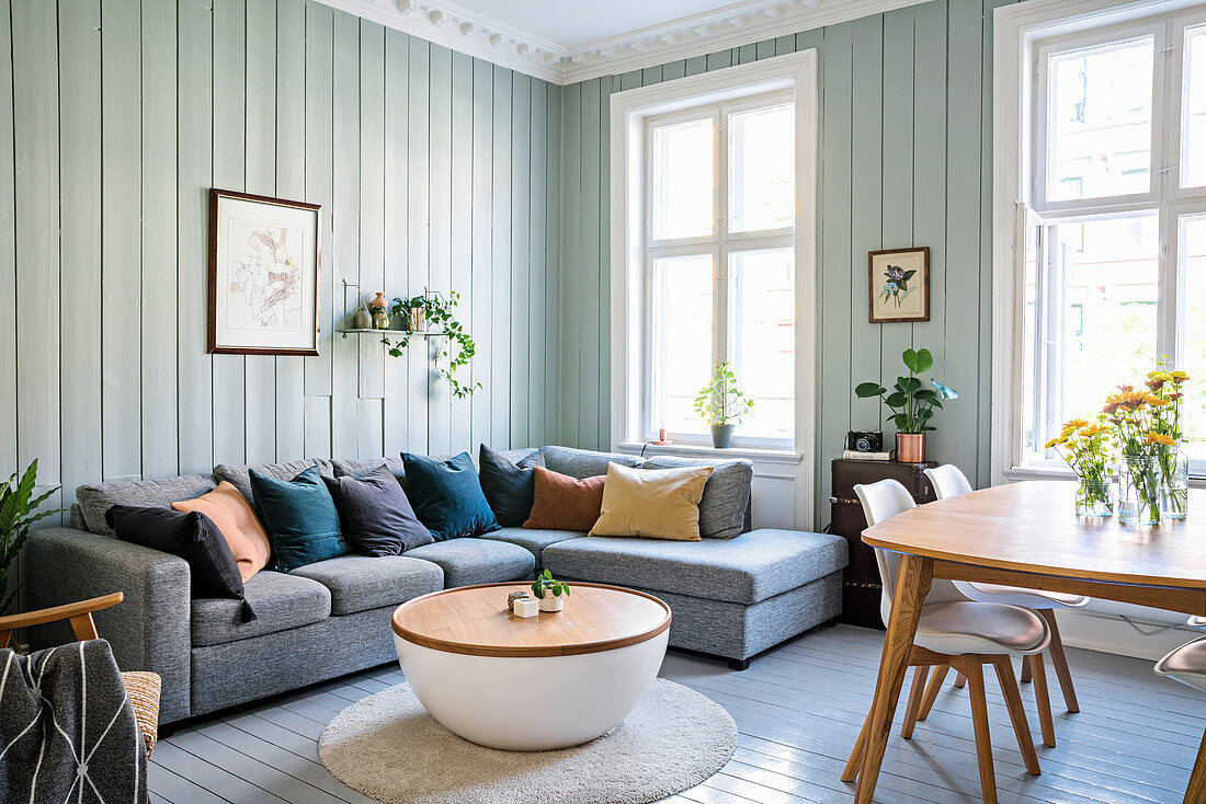 Grey sofa set, coffee table and dining area in living room with wooden walls painted pale green