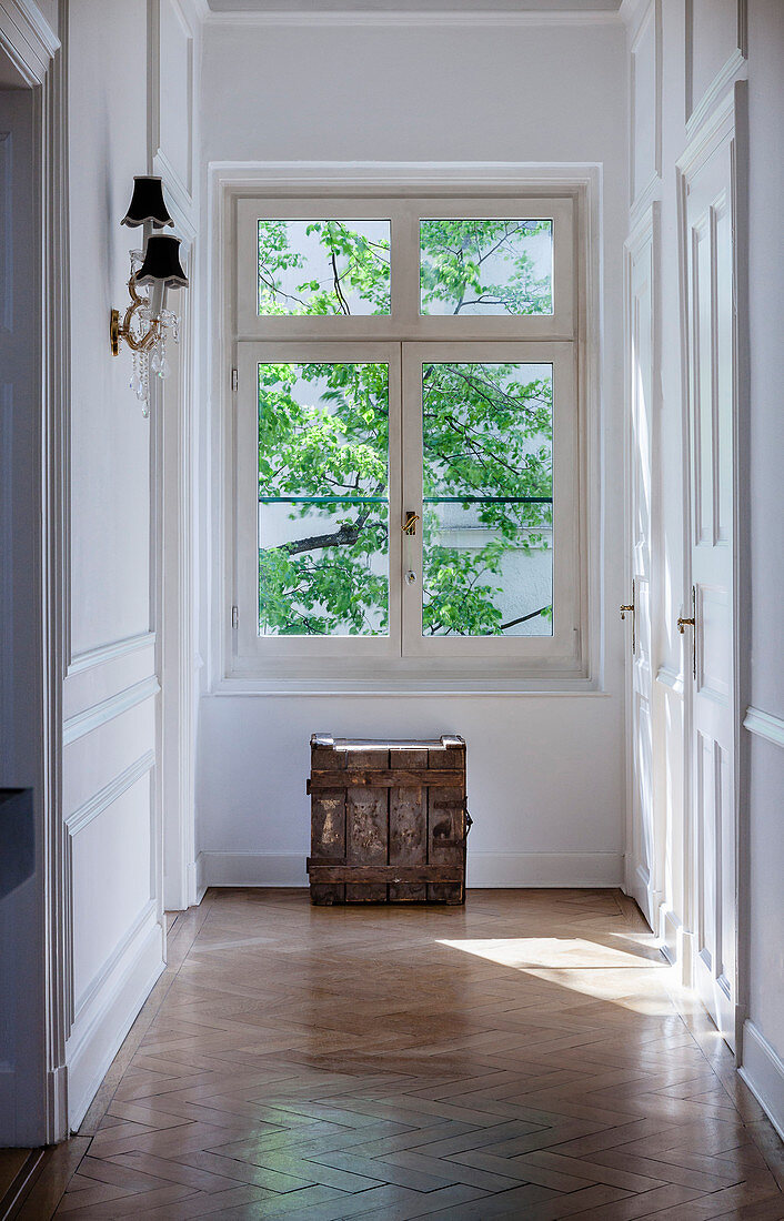 Wooden crate below window in sunny corridor with panelled walls