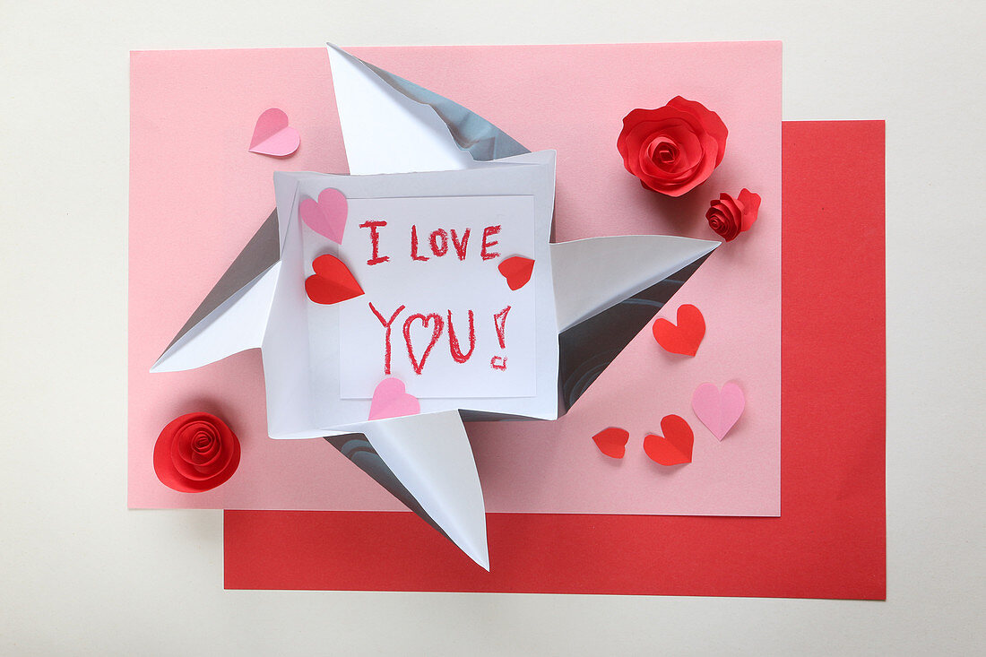 Liebesbotschaft im Origami-Umschlag auf Papier in Rosa und Rot