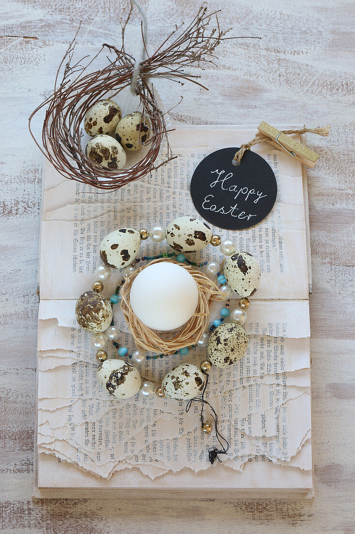Wreath of beads and quail eggs on book with torn pages