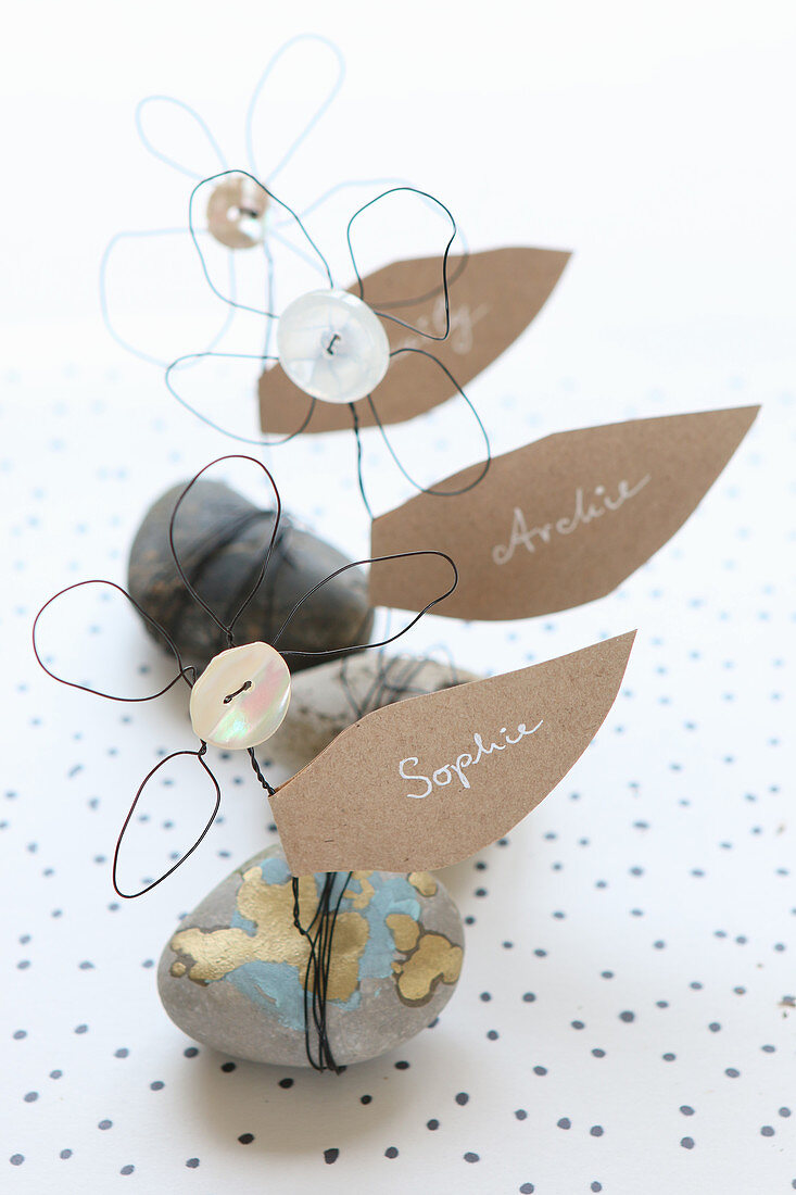 Name cards shaped like leaves on wire flowers on pebbles