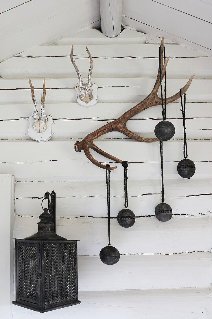 Black baubles, antlers and lantern on wall of log cabin