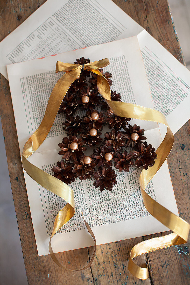 Christmas-tree shape made from pine cones and beads with gold ribbon on book pages