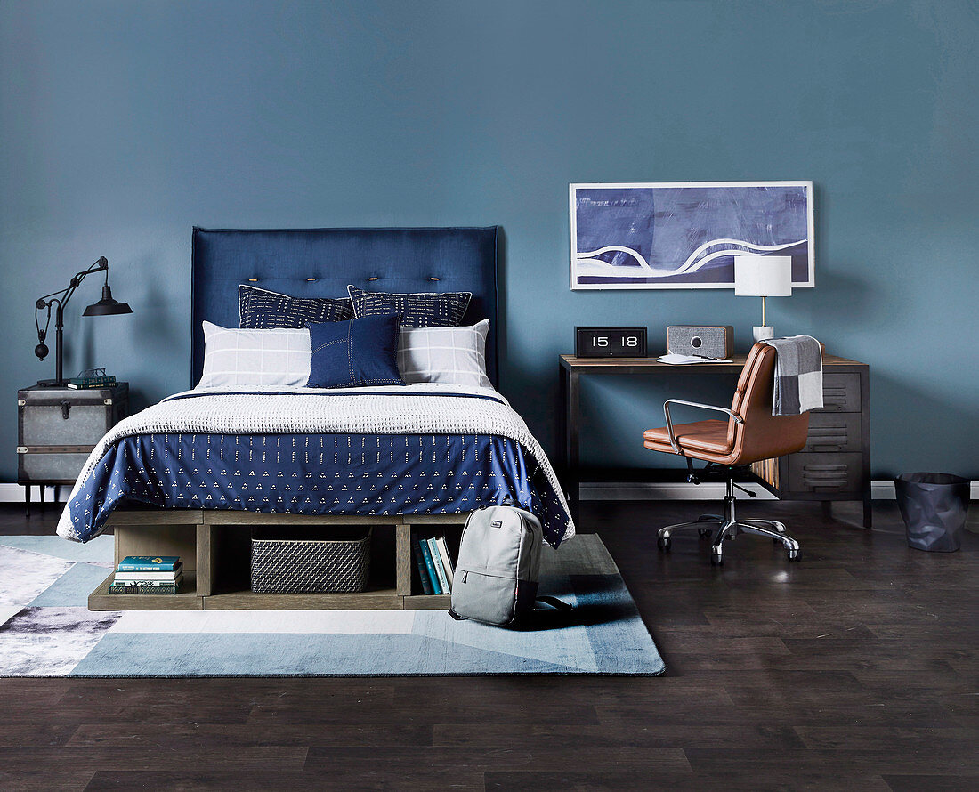Doppelbett mit blauem Betthaupt, daneben Schreibtisch mi Lederstuhl vor blauer Wand