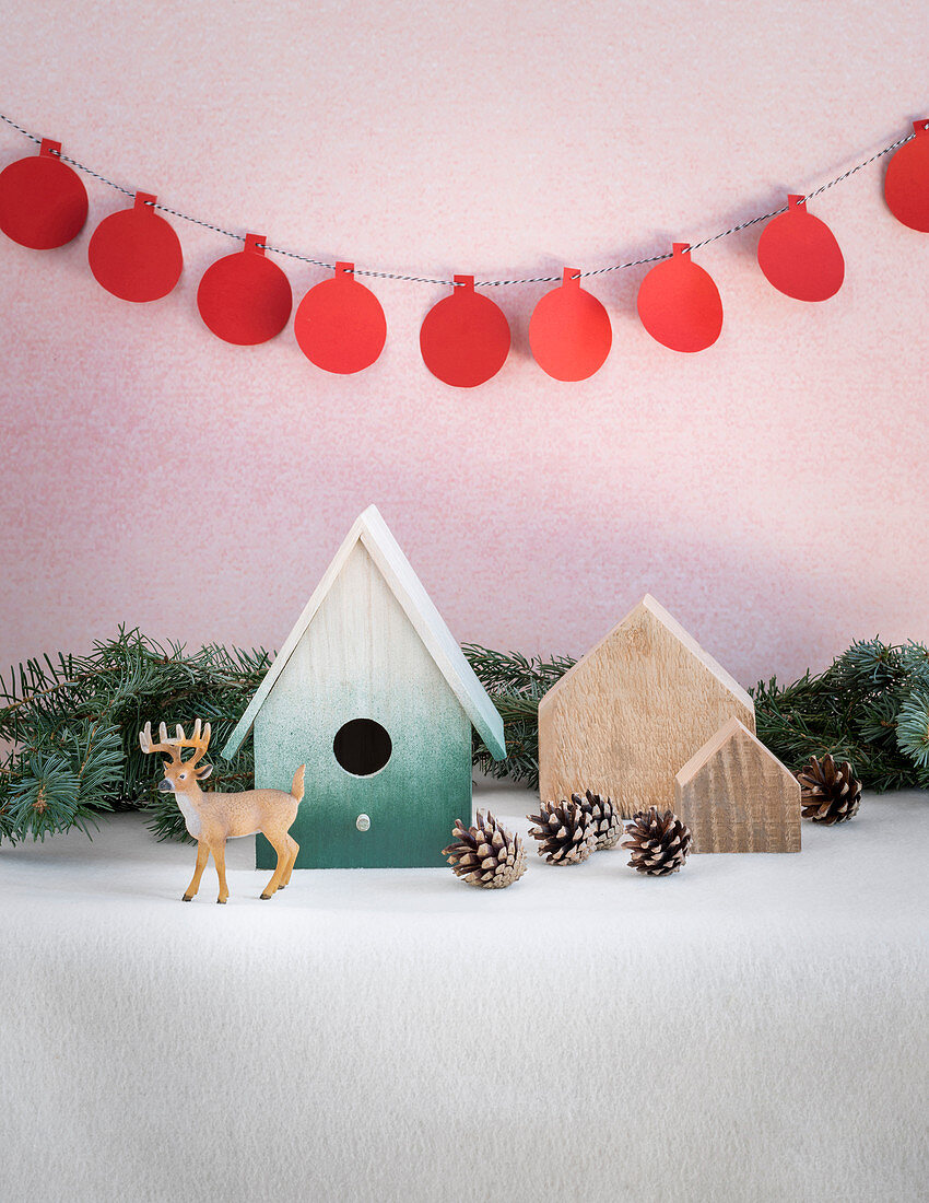 Winter arrangement of nesting box, fir cones, reindeer figurine and garland
