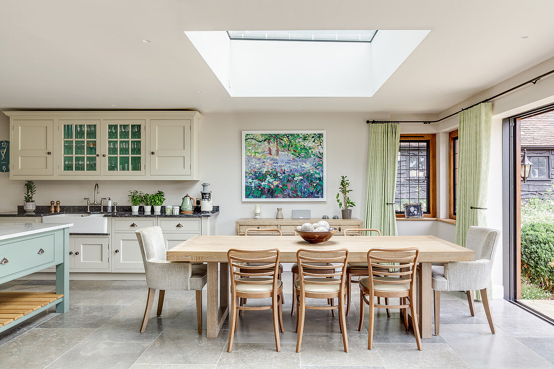 Dining table below skylight and country-house kitchen in open-plan interior