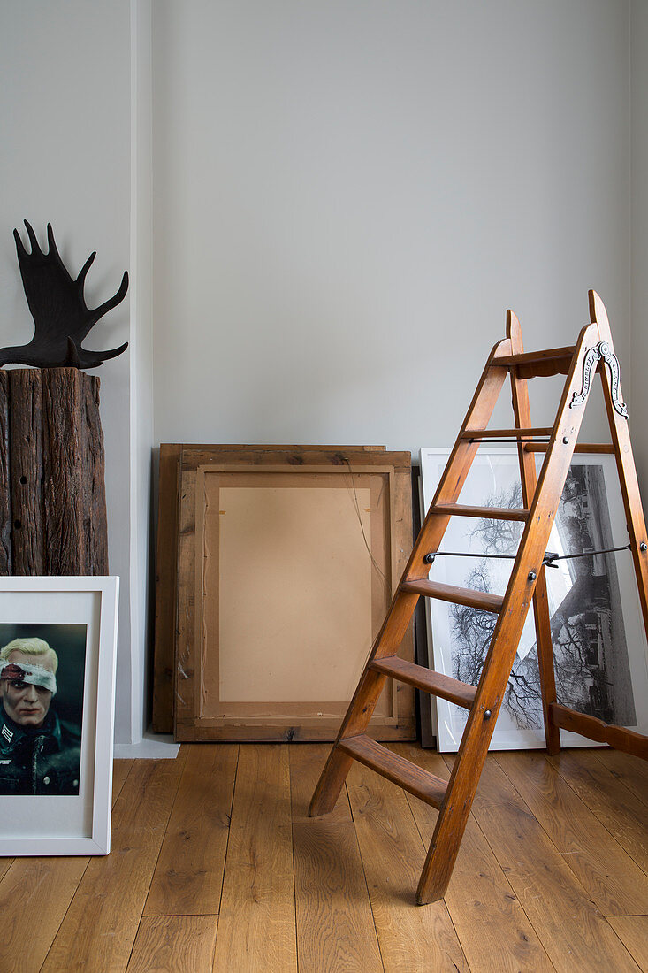 Old wooden stepladder in front of pictures leaning against grey wall