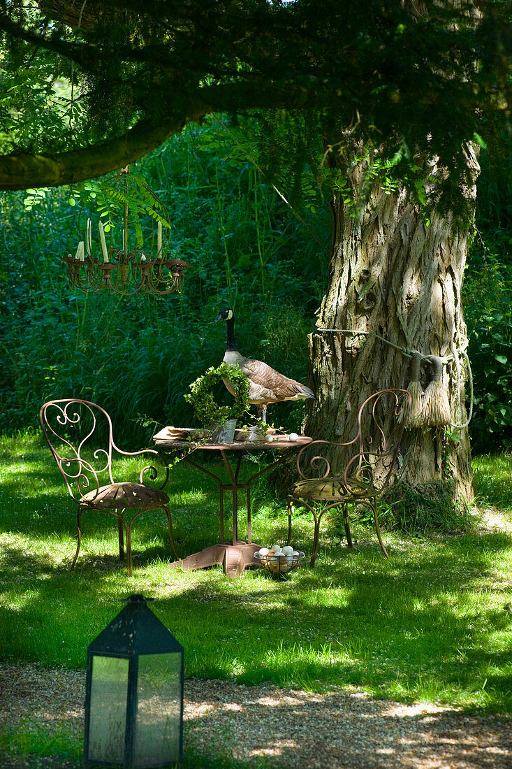Romantischer Gartenplatz mit verschnörkelten Metallgartenmöbeln unter altem Baum