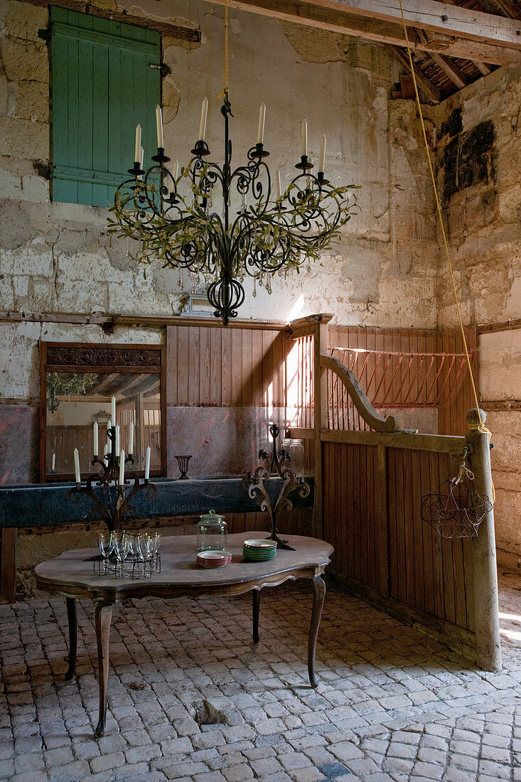 Kronleuchter und antiker Tisch mit Kerzenleuchtern in altem Stallgebäude