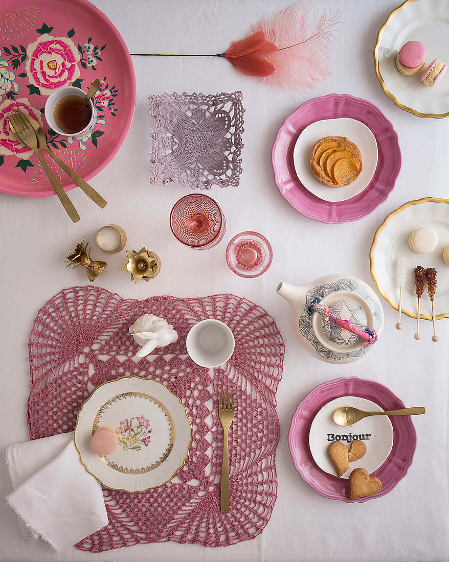 Table set for tea decorated with vintage-style crocheted doilies and floral plates in shades of dusky pink
