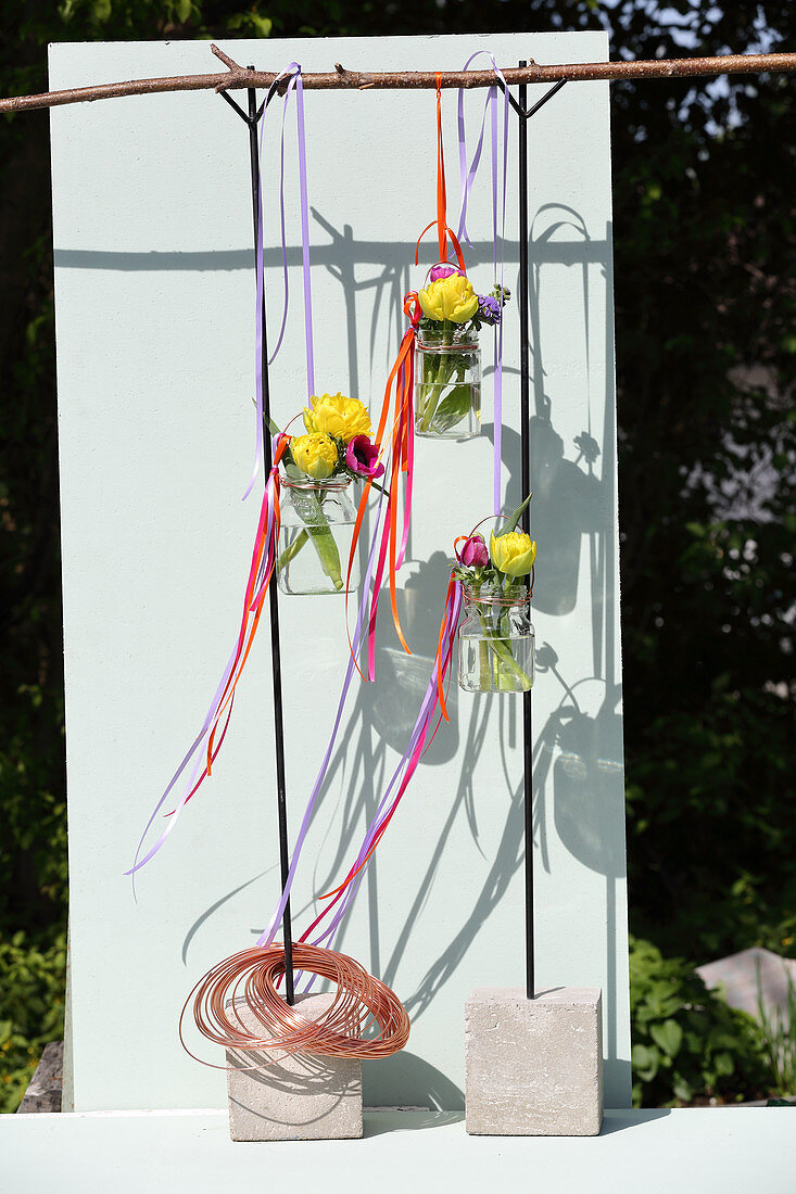 Schraubgläser mit Blumen und bunten Stoffbändern hängen am Ast