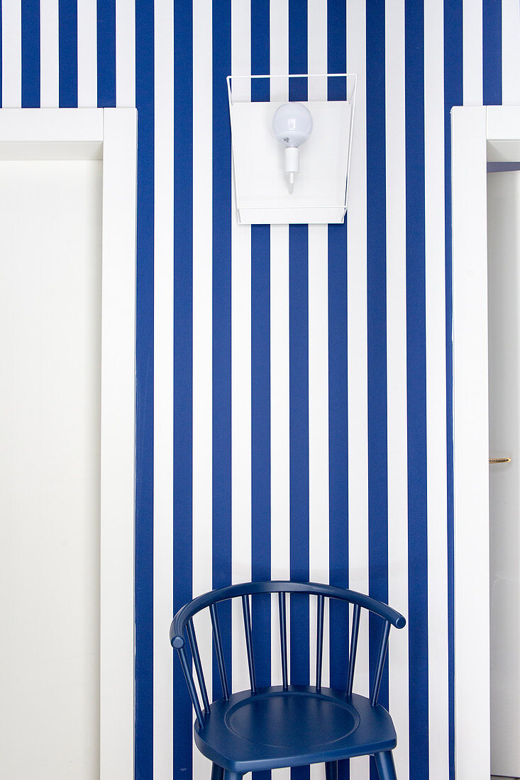 Dunkelblauer Stuhl vor blau-weiß gestreifter Wandtapete