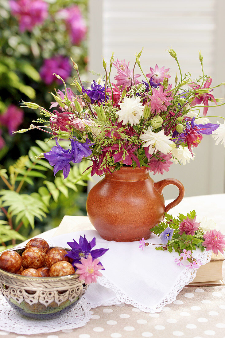 Bouquet of mixed aquilegias and bowl of pastries on terrace table