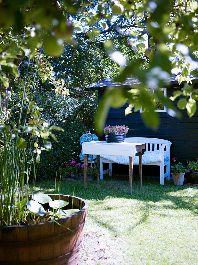 Sitzplatz auf Rasenfläche am Gartenhaus, Holzfass als Mini-Teich