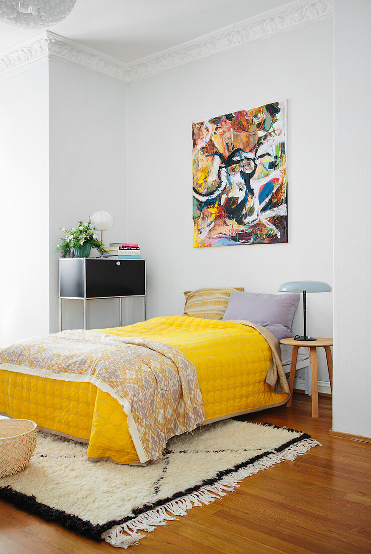 Doppelbett mit gelber Tagesdecke, darüber moderne Malerei im Schlafzimmer