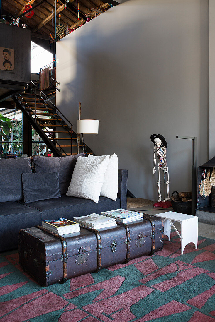 Vintage trunk used as coffee table, sofa and skeleton figurine in front of staircase