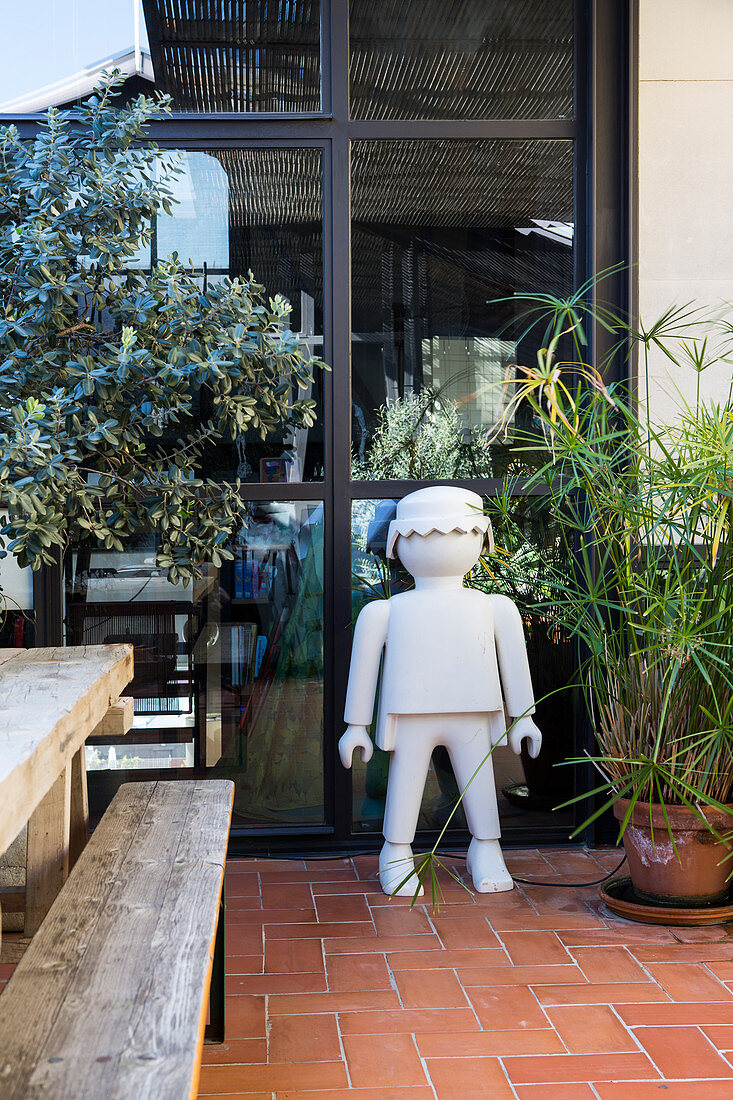 Giant Lego man next to plant on terrace with terracotta floor tiles