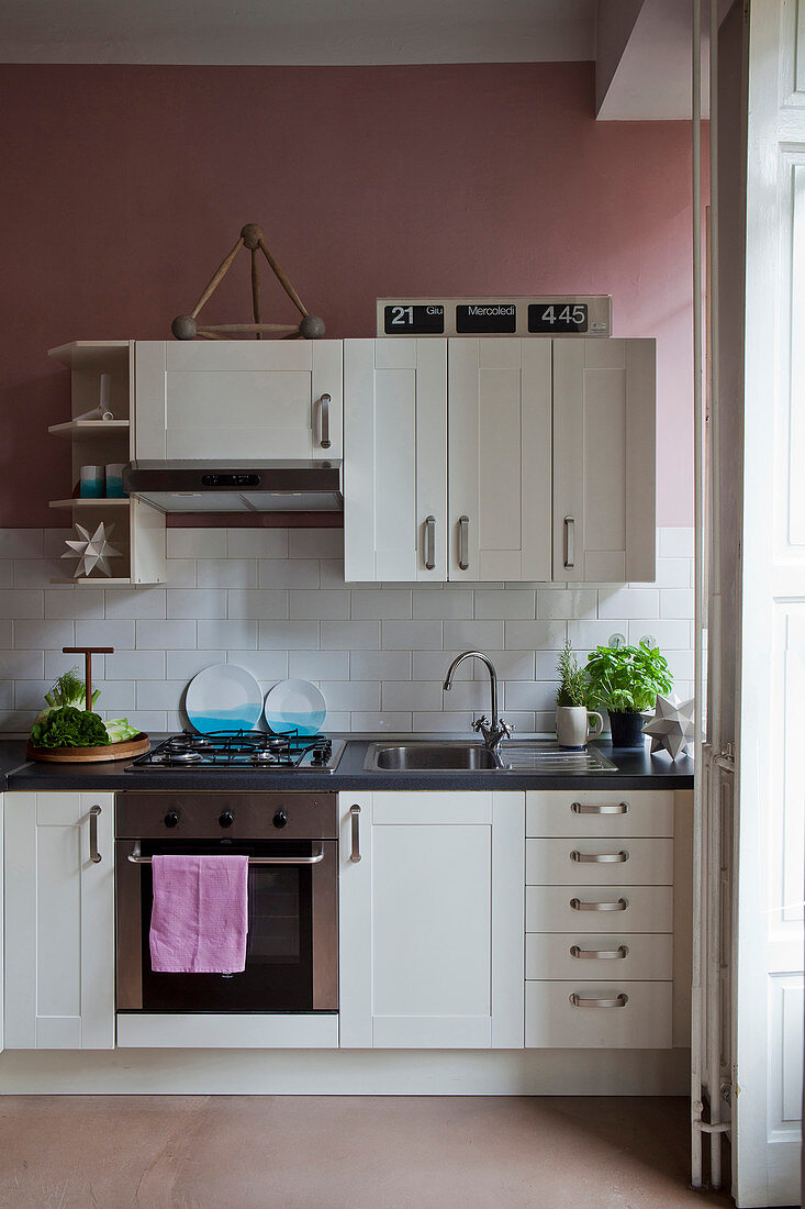 Kitchen with white cupboards, subway tiles and dusky-pink walls in period apartment