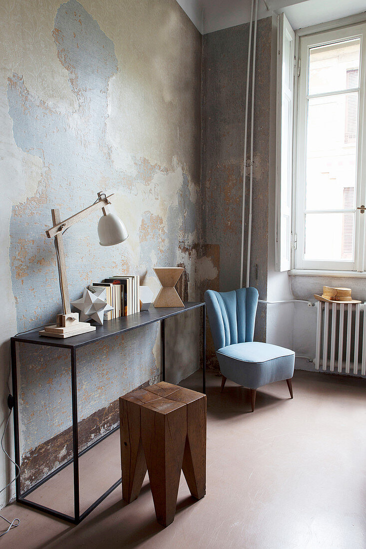 Holzhocker vor schlichtem Metall-Konsolentisch daneben hellblauer Sessel in Altbauwohnung