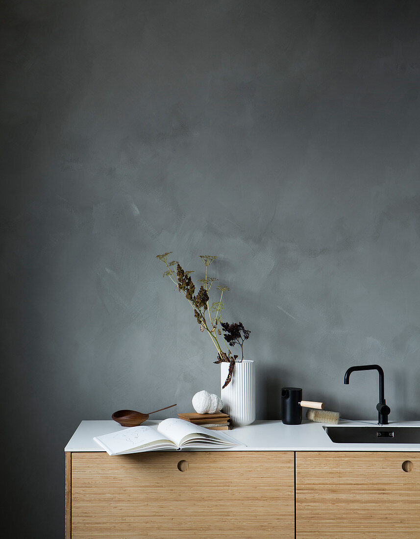 Aufgeschlagenes Buch auf minimalistischer Küchenzeile vor grauer Wand
