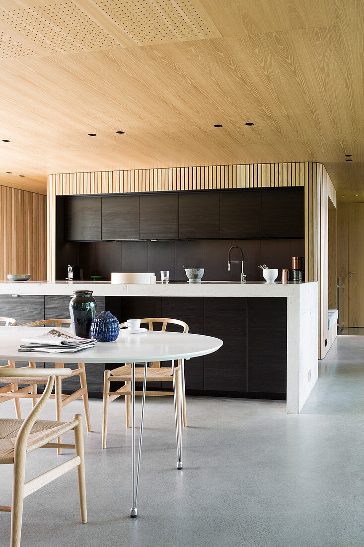 Dining table and designer chairs in front of open-plan kitchen in architect-designed house
