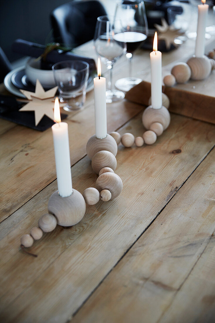 Festively set table decorated with garland of wooden baubles holding candles