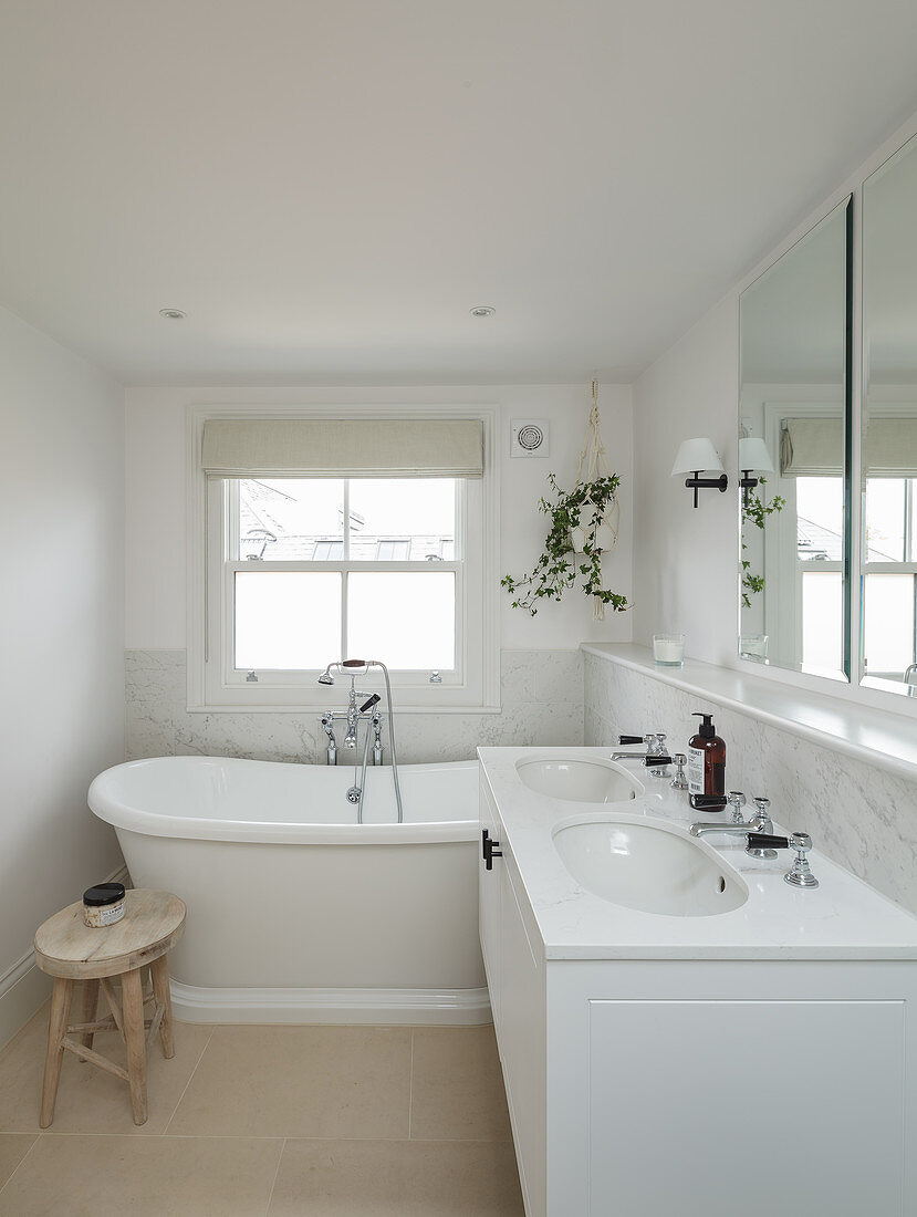 White bathroom with twin washstand and bathtub below lattice window