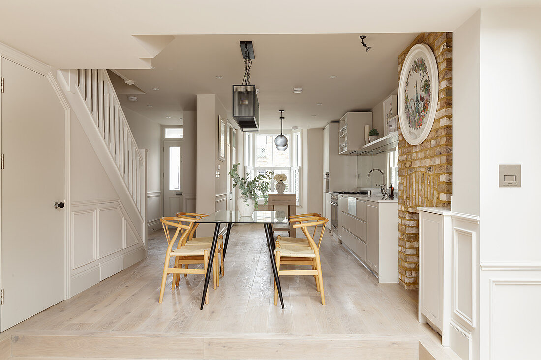 White kitchen and dining area on raised level in elongated, open-plan interior