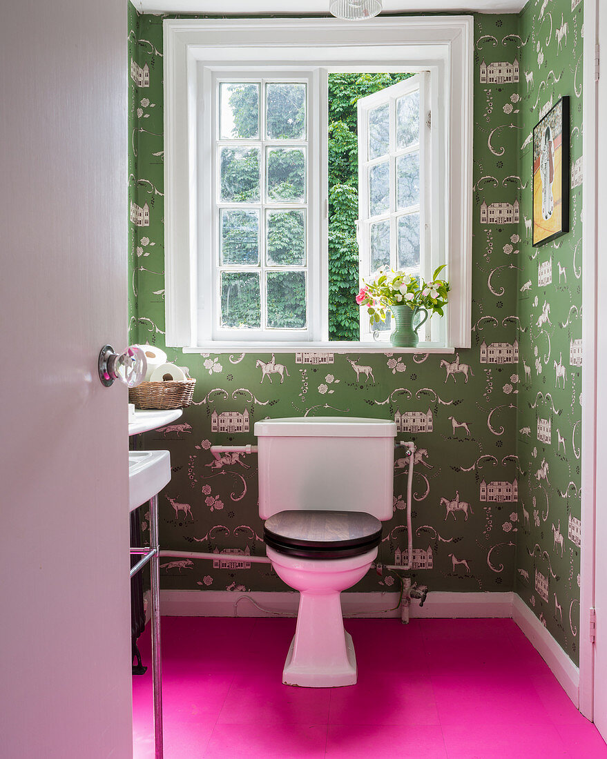 Toilet in small bathroom with hot-pink floor and green wallpaper