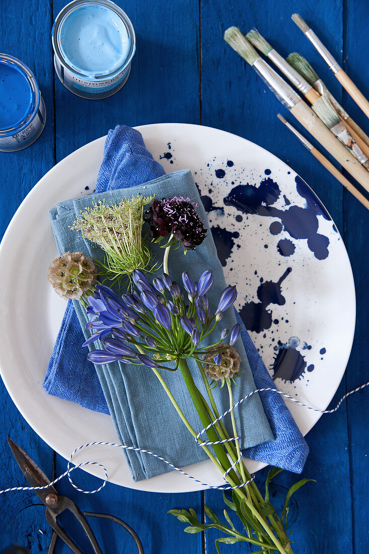 Schmucklilie, Skabiose und blaue Servietten auf gesprenkeltem Teller