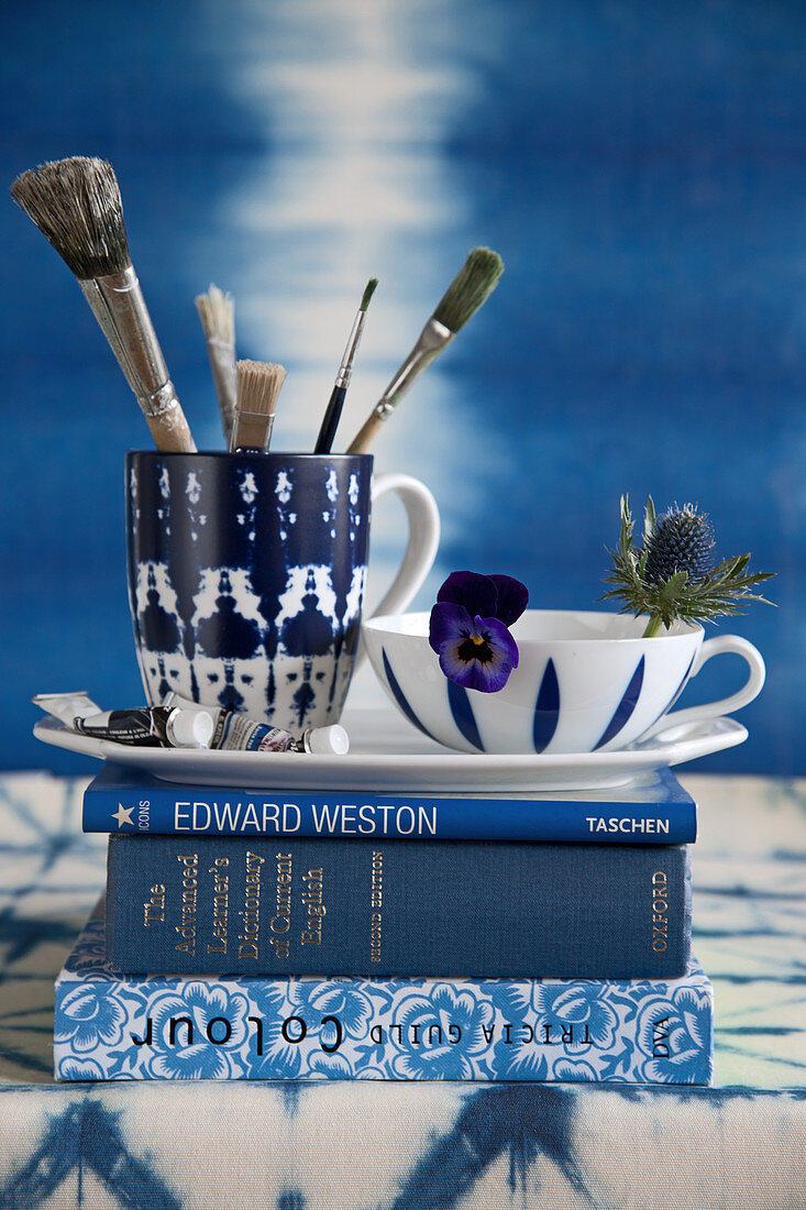 Tassen mit Pinseln und Blumen auf einem Stapel blauer Bücher