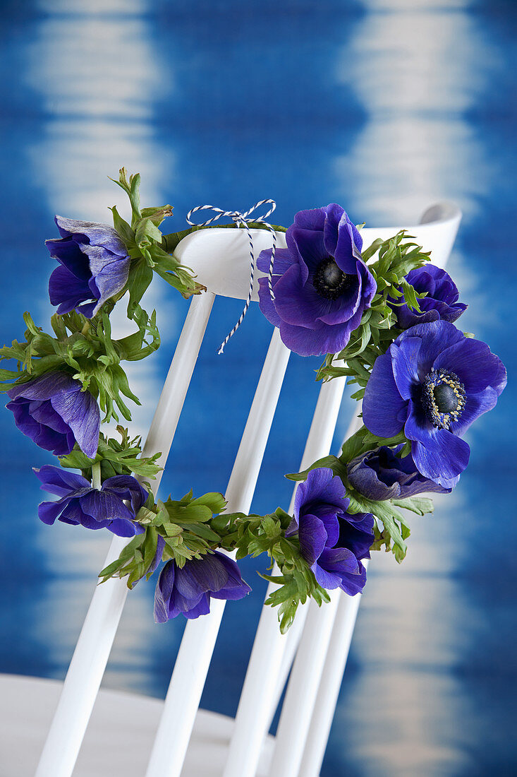 Wreath of anemones hung on backrest of white spoke-back chair in front of blue wall