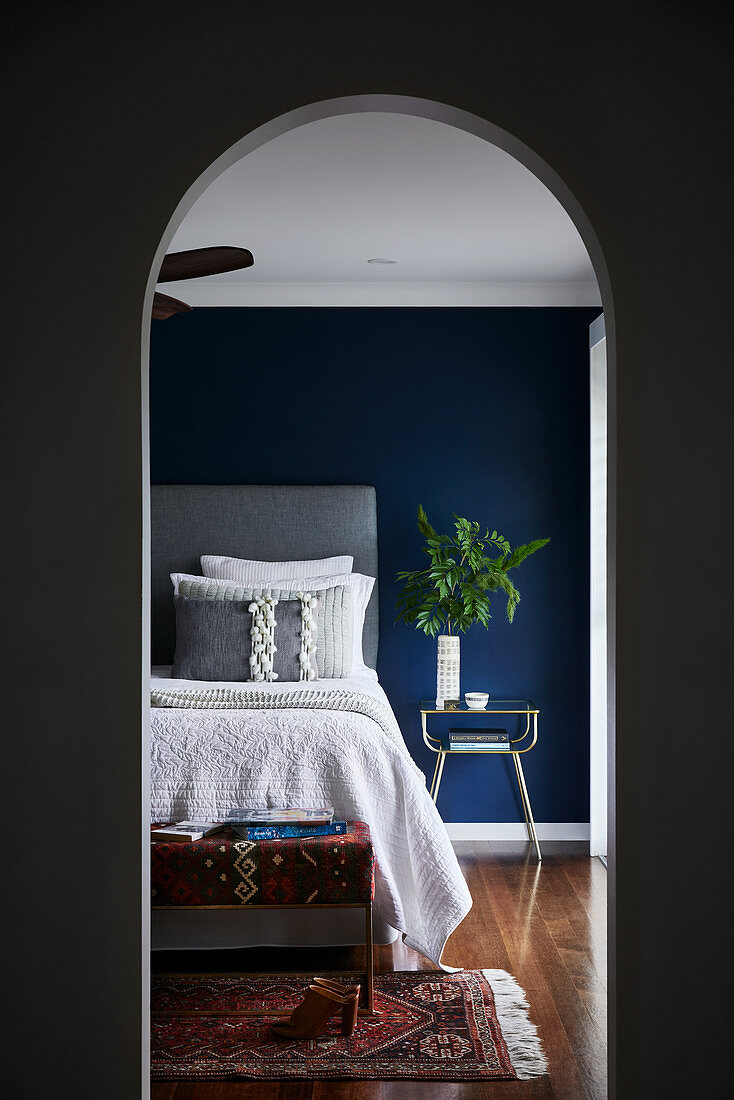 Blick durch Rundbogenausschnitt auf Bett vor petrolfarbener Wand
