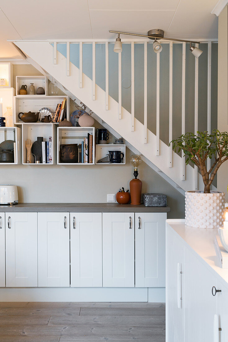Sideboard and shelving modules on wall below staircase in white interior