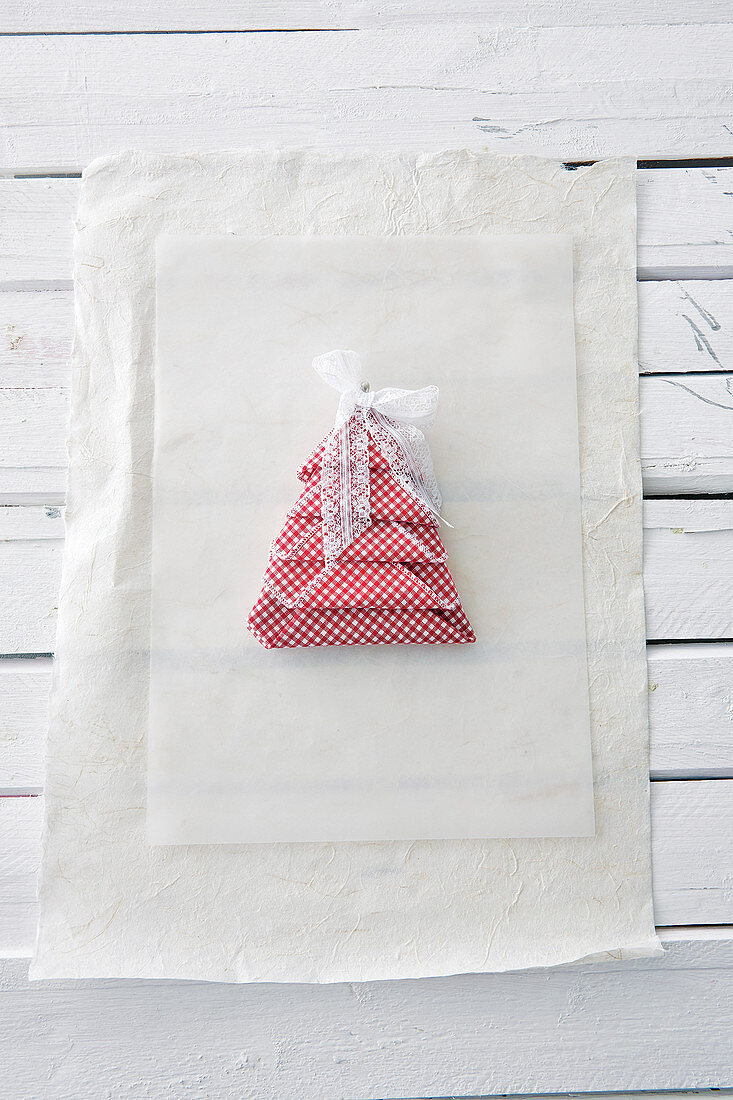 Linen napkin folded into Christmas-tree shape and decorated with lace ribbon