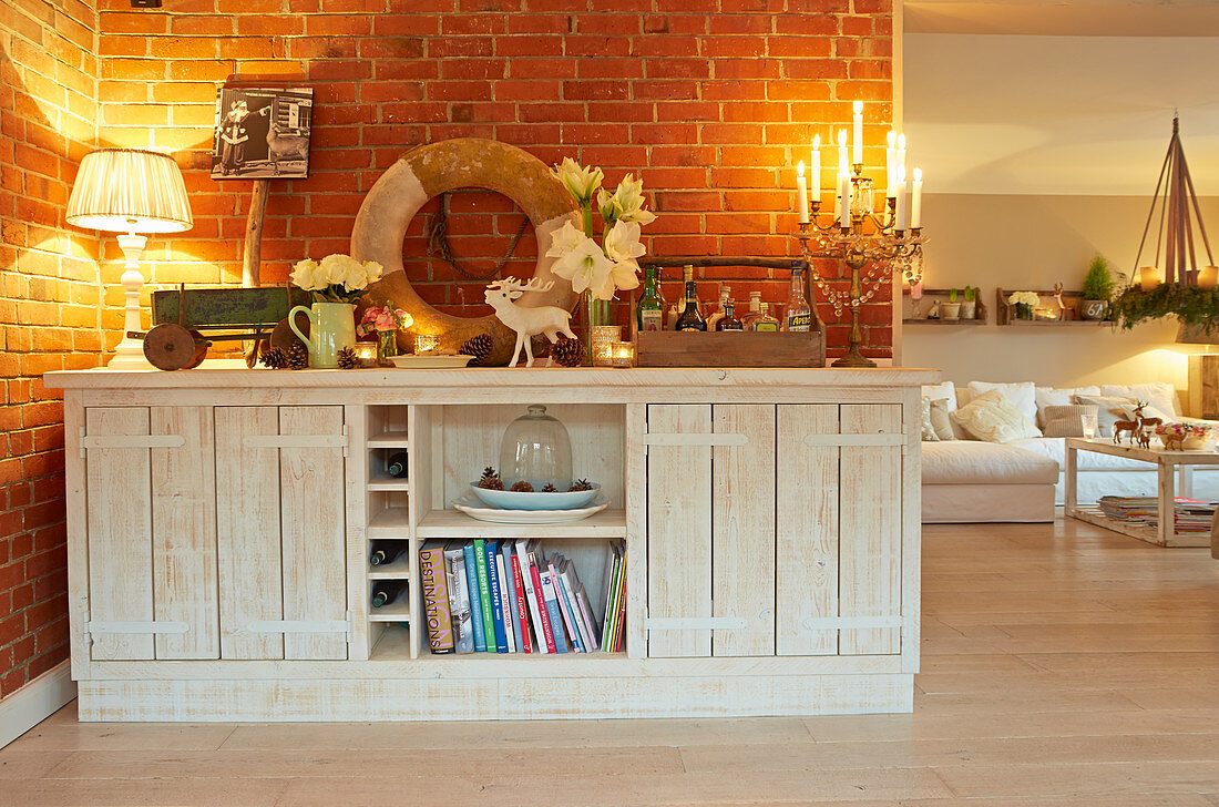 Festively decorated, rustic, white sideboard against brick wall in cosy interior