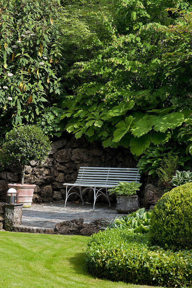 Bench against rustic stonewall in lush, green, well-tended garden