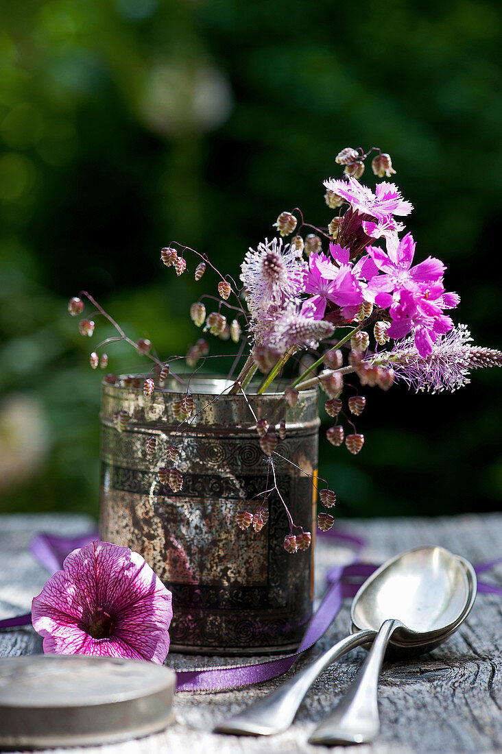 Sträußchen aus Lichtnelke, Wegerichblüten und Plattährengras in alter Teedose, Petunien-Blüte, Löffel