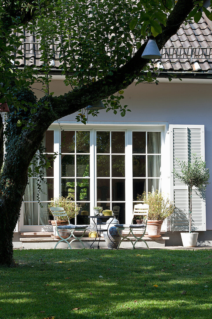 Sitzplatz im sommerlichen Garten vorm Haus mit Sprossenfenstern
