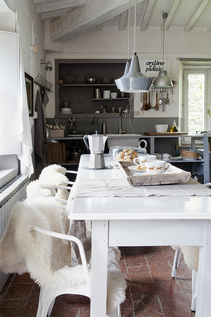Stühle mit Fellen am weißen Esstisch vor rustikaler offener Küche