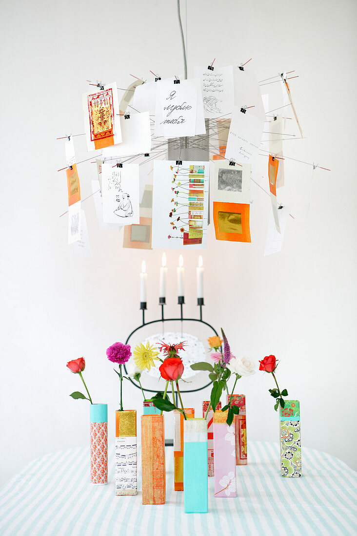 Designerleuchte mit Postkarten über bunten Vasen mit einzelnen Blumen