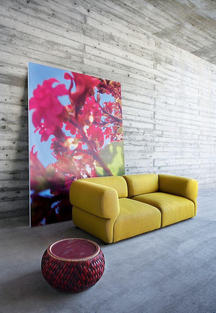 Roter Sitzpouf und senffarbenes Outdoor-Sofa vor großformatiger Blumenfotografie