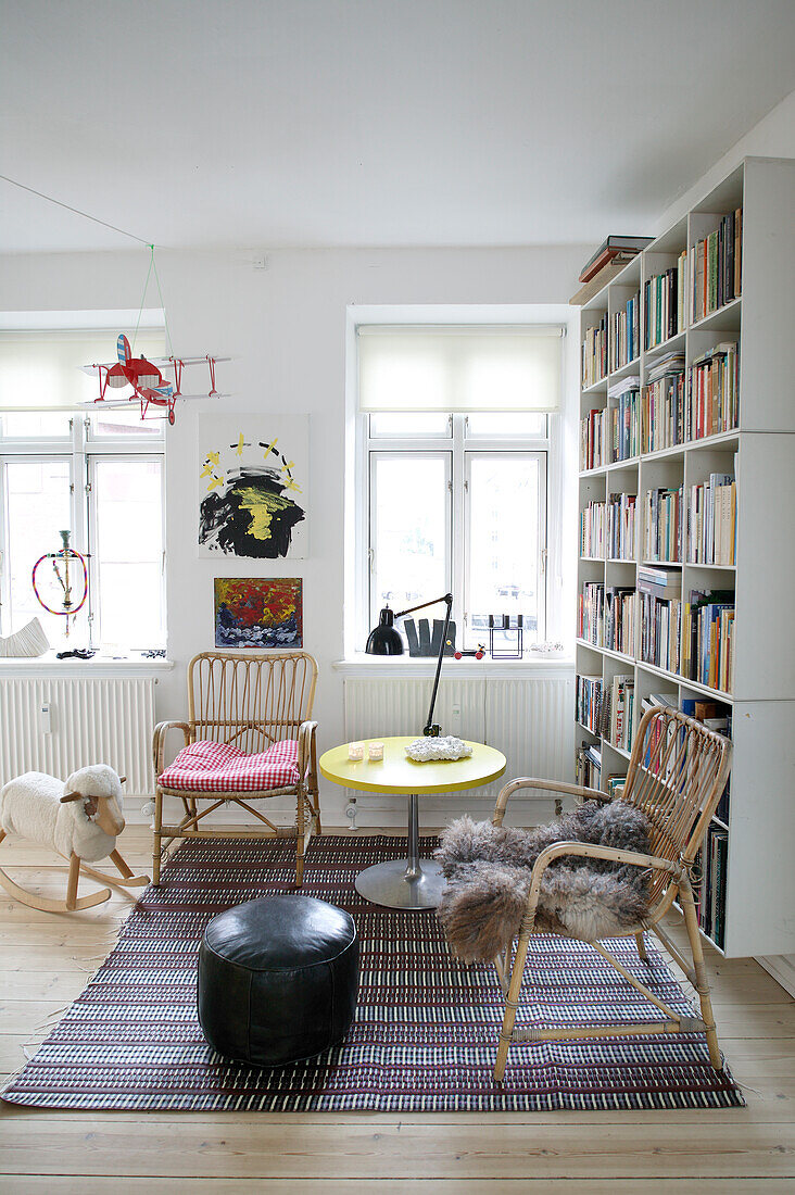 Bücherregal, Rattansessel, Beistelltisch und Pouf und Schaukelschaf im Wohnzimmer