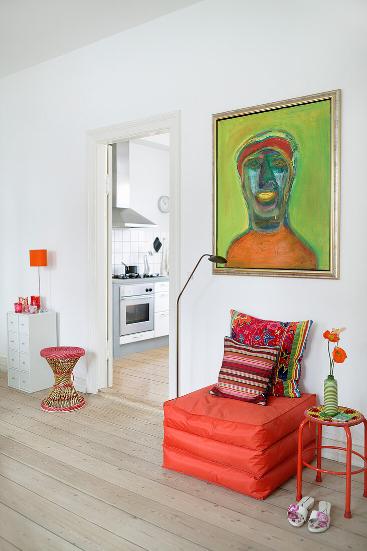 Sitzpouf in Orange unterm grünen Gemälde im Wohnzimmer