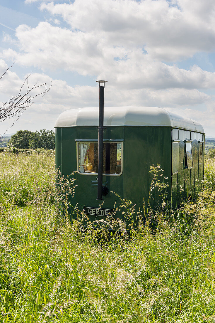 Nostalgischer grüner Wohnwagen mit Kamin in sommerlicher Wiese