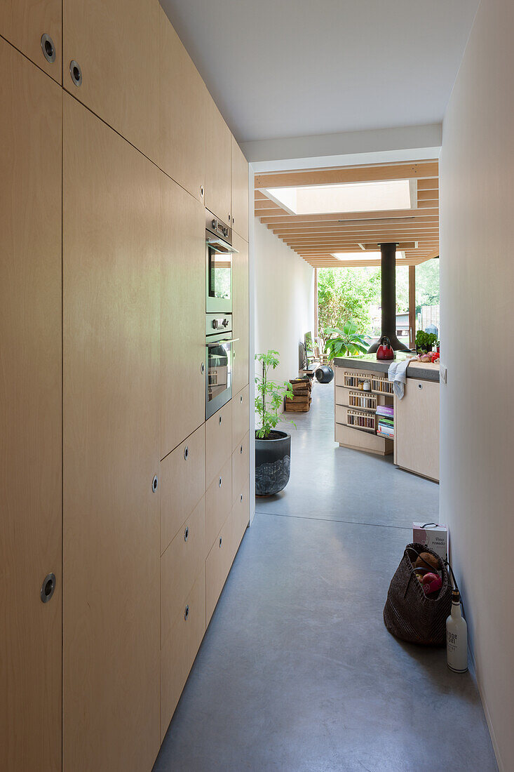 Moderne Küche mit raumhohen Einbauschränken aus hellem Holz und grauem Boden